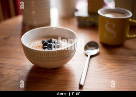 Dampfende Schüssel Haferbrei in Tabelle Frühstücksszene mit Tasse Tee. Stockfoto