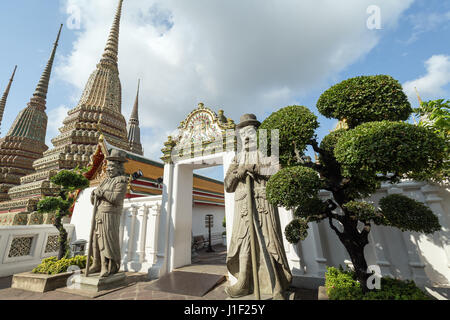 Zwei große chinesische Statuen, Bäume, Tor und Chedis in der Tempelanlage Wat Pho (Po) in Bangkok, Thailand. Stockfoto