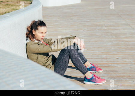 Junge attraktive Frau Sportswear im Freien sitzen und ruhen Sie sich nach sportlichen Übungen an einem sonnigen Morgen Stockfoto