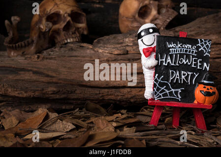 Mumie und Jack-o-Laterne stehend auf willkommen Halloween Party Board mit menschlicher Schädel und welkes Blatt im Wald Stockfoto