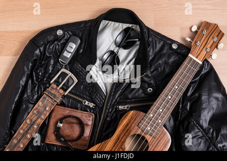 Schwarze Jacke mit Herren Accessoires und Ukulele auf Holztisch Stillleben Stil Stockfoto