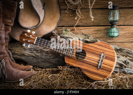 Gemälde Stillleben mit Ukulele auf amerikanischen Westens Rodeo braunen Filz Cowboy-Hut und traditionellen Leder Stiefel in Vintage Ranch Scheune staatlich Stockfoto