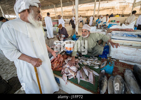 Muscat, Oman - Muttrah Corniche (Uferpromenade) Mann bespricht Fisch mit Kunden im Fischmarkt in Mutrah Fish Market Stockfoto