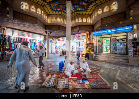 Muscat, Oman - Souq Muttrah Männer sitzen auf Teppich im Markt verkaufen verschiedene traditionelle Elemente Stockfoto