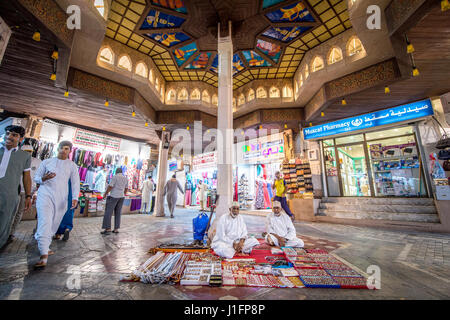 Muscat, Oman - Souq Muttrah Männer sitzen auf Teppich im Markt verkaufen verschiedene traditionelle Elemente Stockfoto