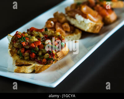 Auswahl an leckere Bruschetta oder Kanapees auf Taosted Baguette mit geräuchertem Chiken, Tomaten, Basilikum und Auberginen Stockfoto