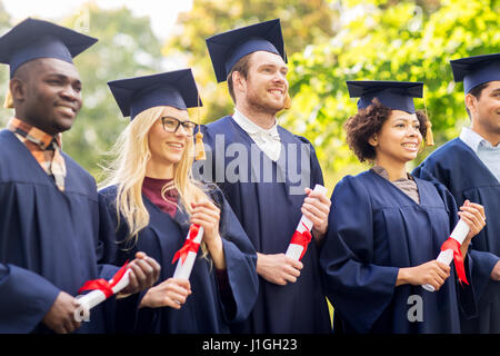 glückliche Schüler in Mörtel-Boards mit Diplomen Stockfoto