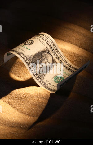 1 Dollar Banknote auf Sand mit langen Schatten Stockfoto