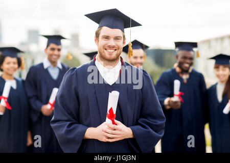 glückliche Schüler in Mörtel-Boards mit Diplomen Stockfoto