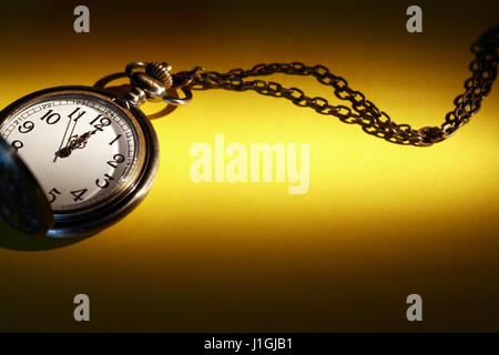 Vintage Taschenuhr mit Kette auf gelbem Papieroberfläche unter Strahl des Lichts Stockfoto