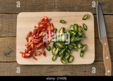 Chili Paprika rot und Grün in Scheiben und Messer auf Schneidebretter im Hintergrund Tisch Holz. Stockfoto