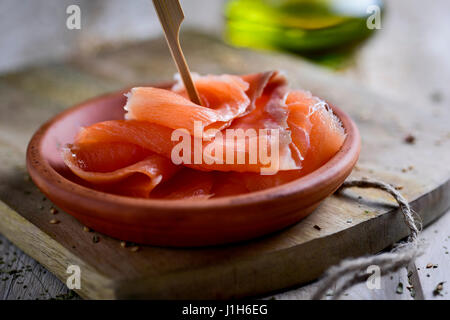 Nahaufnahme von einem Steingut-Schale mit einigen Scheiben vom geräucherten Lachs auf eine rustikale Schneidbrett aus Holz und eine Menage Olivenöl im Hintergrund Stockfoto