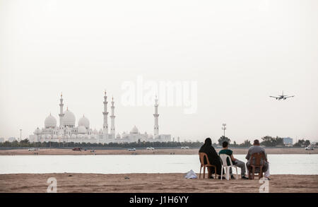 ABU DHABI, VEREINIGTE ARABISCHE EMIRATE - 27 April, 2012: eine Familie sitzt am Wasser mit Blick auf die Sheikh Zayed Moschee in Abu Dhabi. Stockfoto