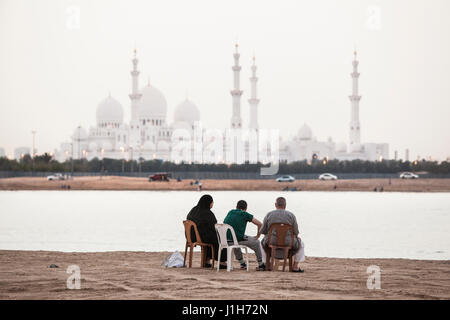 ABU DHABI, VEREINIGTE ARABISCHE EMIRATE - 27 April, 2012: eine Familie sitzt am Wasser mit Blick auf die Sheikh Zayed Moschee in Abu Dhabi. Stockfoto