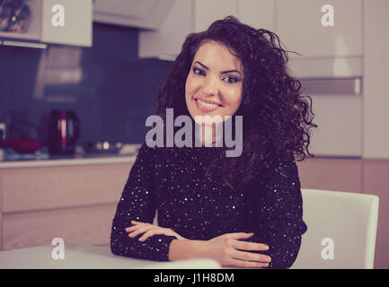 Glückliche Frau lächelt in die Kamera beim Sitzen zu Hause in der Küche Stockfoto