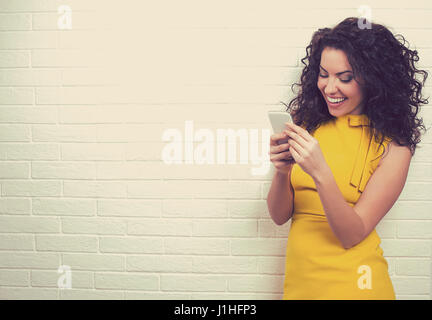 Porträt von attraktiven Frau mit High-Speed-Internet-Anschluss, SMS ihre Freunde über soziale Netzwerke auf Smartphone gegen Mauer isoliert Stockfoto