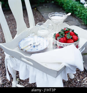 Tablett mit Geschirr und Erdbeeren auf Stuhl. Stockfoto