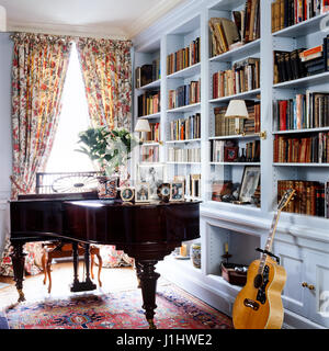 Klavier und Gitarre neben Bücherregal. Stockfoto