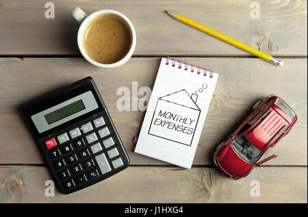 Notizblock mit Budget handschriftlich innerhalb einer Skizze eines Hauses mit einem Miniatur-Auto und Rechner Stockfoto