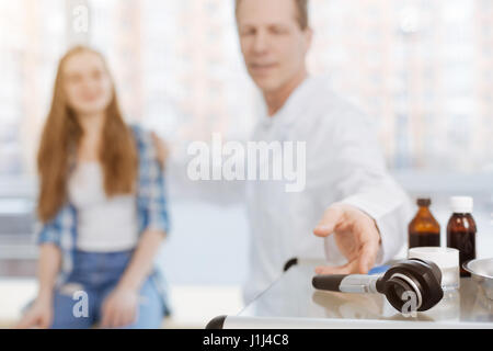 Lächelnd Arzt mit Dermatoskop bei Patienten Besuch am Arbeitsplatz Stockfoto