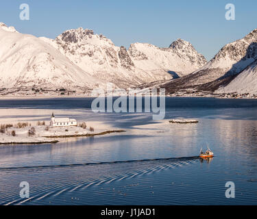 Sildpollnes Kirche mit einem vorbeifahrenden roten Fischerboot auf Austvagoya, Lofoten Inseln, Norwegen Stockfoto