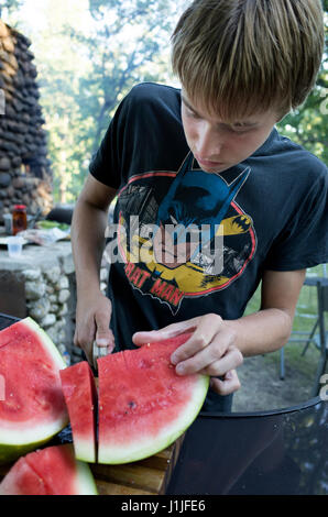 Teenboy in Batman T-shirt Schnitt Scheiben Wassermelone außerhalb. Clitherall Minnesota MN USA Stockfoto