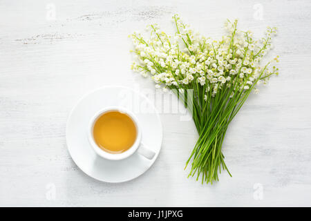 Tasse Tee und Strauß Maiglöckchen am rustikalen Tisch. Stockfoto