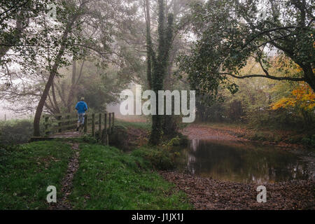 Mann zu Fuß auf einer Brücke über einen Fluss im Nebel. Norfolk, Großbritannien. Stockfoto