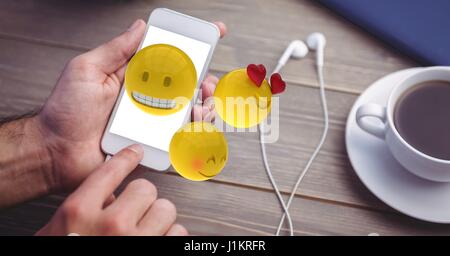 Digital Composite Hände mit Emojis auf Smartphone von Kopfhörer und Kaffeetasse am Tisch Stockfoto