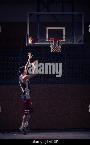 Ein junger Erwachsener Mann, Basketball-Spieler schießen, Ball in der Luft, drinnen vor Gericht Stockfoto