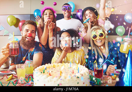 Streamer umgebenden Gruppe von fröhlichen Freunde feiern eine Party mit großen Kuchen und Getränke am Tisch im Vordergrund Stockfoto