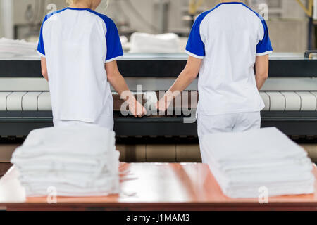 Wäsche-Arbeiter stellt gebügelt Textil in Bügeln Maschine Stockfoto