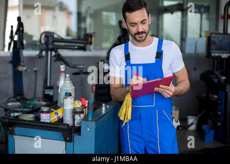 Konzentrierte Mechaniker schreiben über Zwischenablage in der Reparatur-Werkstatt Stockfoto