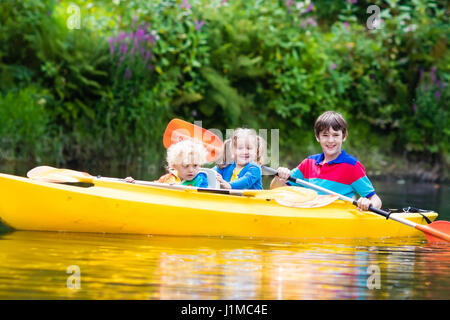 Glückliche Familie mit drei Kindern Kajakfahrt auf schönen Fluss genießen. Kleine Mädchen, Kleinkind Jungen und Teenager Kajak an heißen Sommertag. Wassersport und Stockfoto