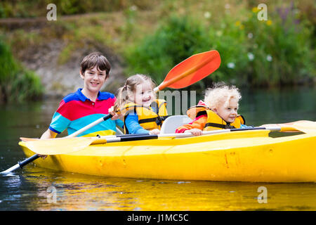 Glückliche Familie mit drei Kindern Kajakfahrt auf schönen Fluss genießen. Kleine Mädchen, Kleinkind Jungen und Teenager Kajak an heißen Sommertag. Wassersport und Stockfoto