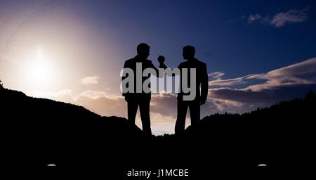 Digitalen Verbund von Geschäftsleuten, die Hand in Hand gegen Himmel auf Bergen Stockfoto