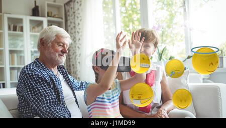 Digital Composite Digital zusammengesetztes Bild von Emojis fliegen von Familie während Girl mit VR-Brille sitzend auf sofa Stockfoto