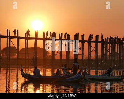 Februar 2017, Mandalay Myanmar - die berühmten u-Bein Brücke mit Menschen zu Fuß über sie während des Sonnenuntergangs mit Touristen auf long-Tail-Boote in der front Stockfoto