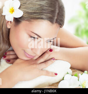 Closeup Portrait von eine schöne Frau im Spa, schöne Welpen mit frischen Frangipani Blume im Haar liegen auf Massagetisch, Verwöhnung und Entspannung Stockfoto