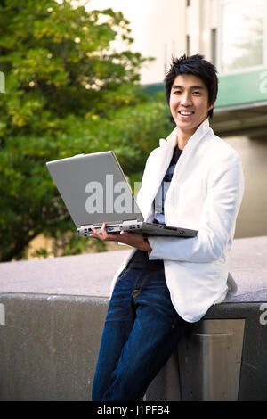 Eine asiatische Studentin hält einen Laptop auf dem campus Stockfoto