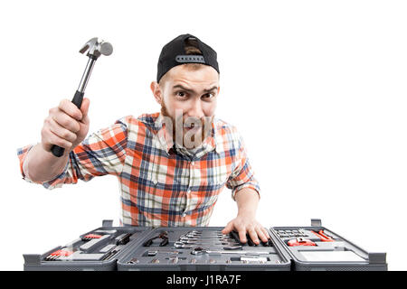 Rothaarige bärtiger Mann trägt einen Baseball-Cap und Shirt mit einem Schraubenschlüssel aus einer Toolbox vor ihm. Isoliert auf weiss. Zimmermannshammer Stockfoto