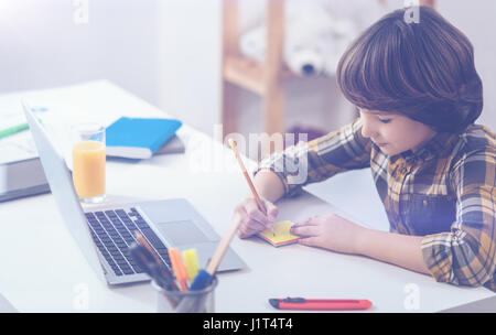 Intelligenter Junge mit Laptop und feststellend, dass während des Studiums Stockfoto