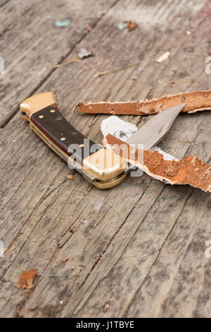 Klappbare Taschenmesser auf Holztisch mit Holzspänen, die es umgibt. Stockfoto