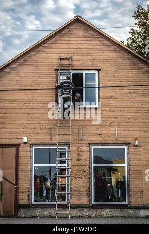 Mann auf Leiter altes Holzhaus mit der Kollegin blickte ihn aus dem Fenster zu reparieren. Stockfoto