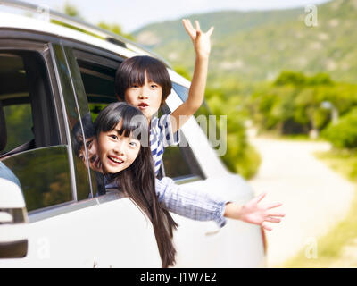 glückliche asiatische Kinder stecken ihre Köpfe aus dem hinteren Fenster während der Fahrt in einem Auto. Stockfoto