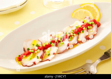 Frisches Sashimi vom Oktopus mit Sauce und Zwiebeln Zitrone auf weißem Teller Stockfoto