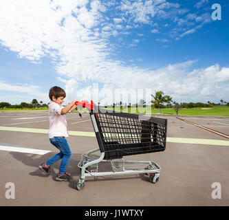 Seite Ansicht Portrait Kind jungen drücken leere Kunststoff Warenkorb auf Parkplatz Stockfoto