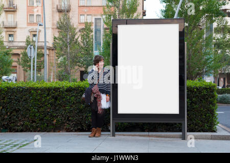 Frau im Gespräch mit Handy, stehend in einer leeren Plakatwand Stockfoto