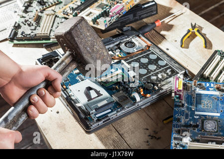Männliche Hände mit Vorschlaghammer Bremsen Laptop und Computer Elektronik Detailansicht. Engineering-humor Stockfoto