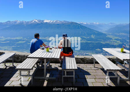 Zwei junge Männer sitzen auf Holzbänken und bewundern das Panorama von der Seegrube Cable Car Station, Innsbruck, Tirol, Österreich Stockfoto